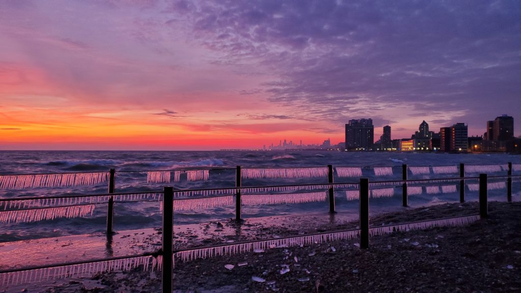 Icicles form on the railing of the lighthouse pier at Loyola Beach at sunrise in Winter, looking south to the Chicago skyline.